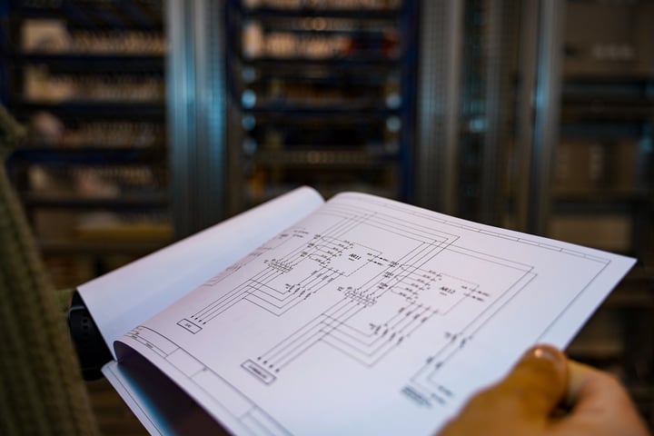 Engineer in an electrical room holding an open set of electrical plans