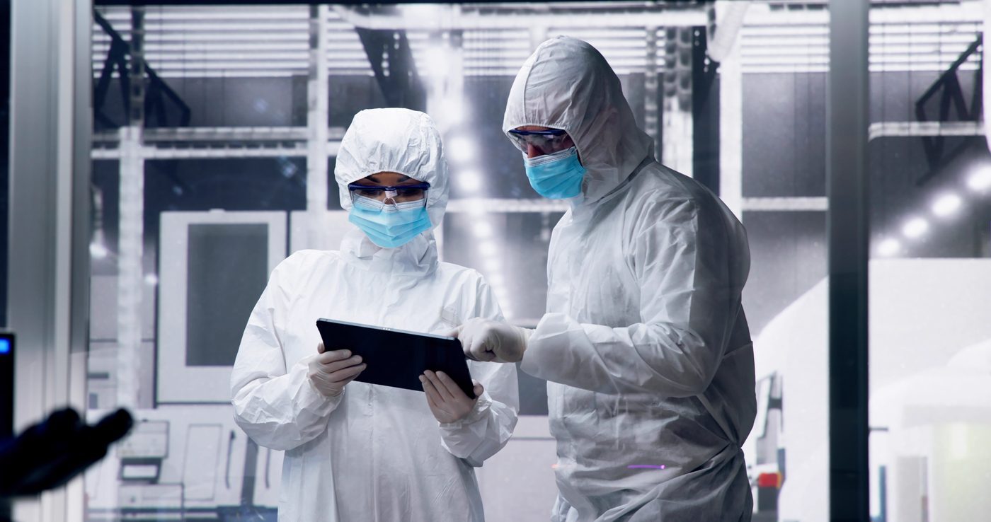 Two engineers in cleanroom suits reviewing a tablet on the fab floor