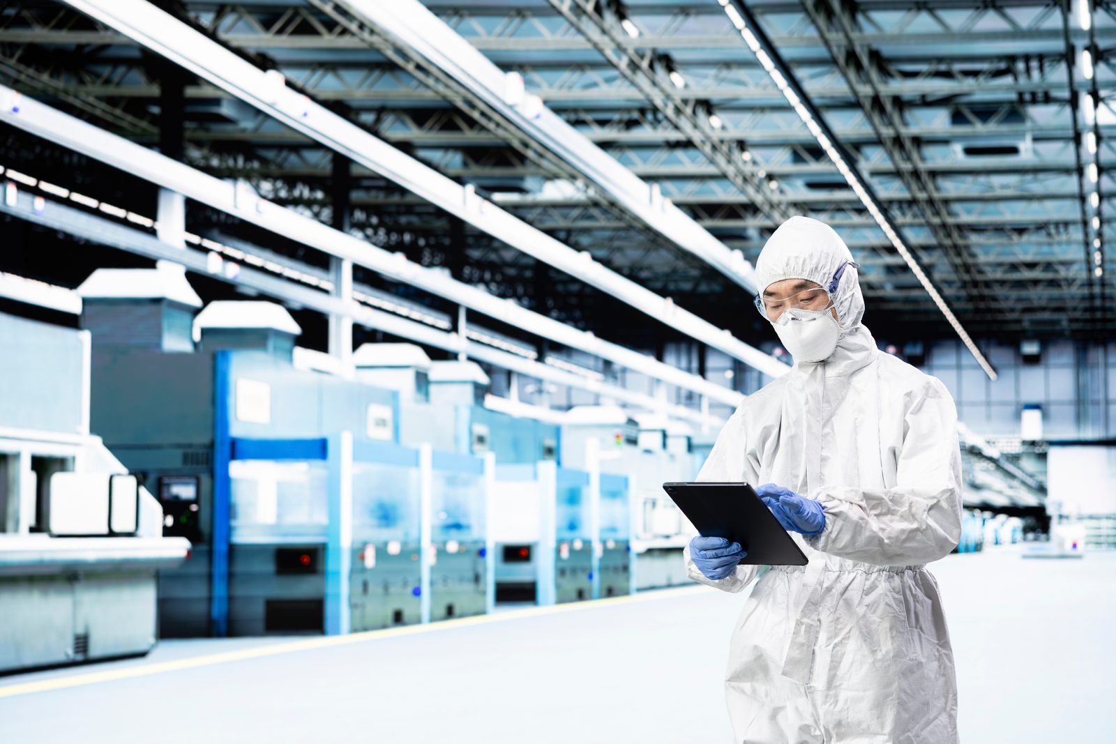 Engineer in cleanroom garments with a tablet walking a row of semiconductor process tools