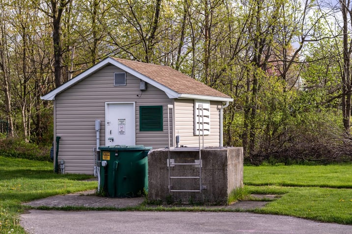 Small sewage pumping station building in the trees with the wet well hatch beside it